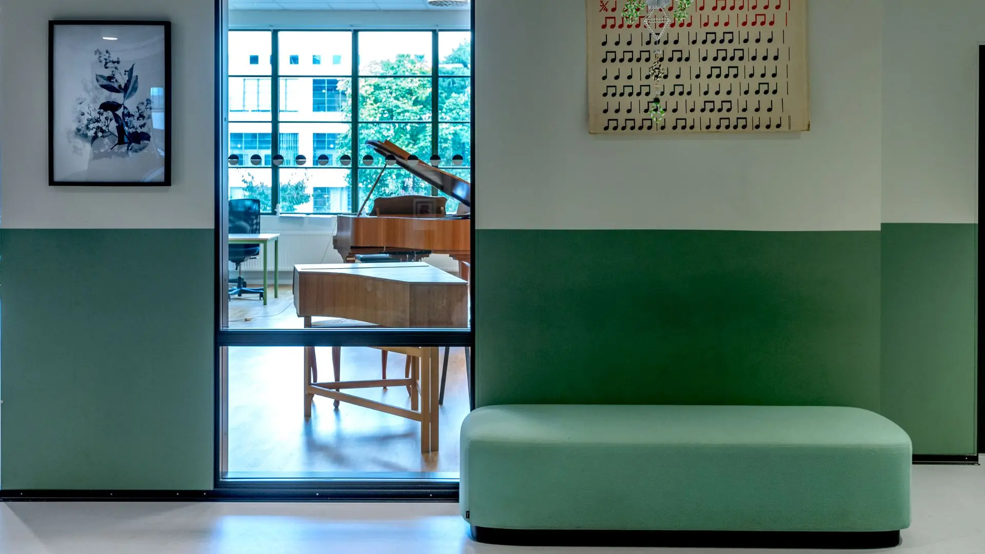 Foto på en grön korridor med en grön puff. Genom ett fönster ser man ett rum med ett piano i. 